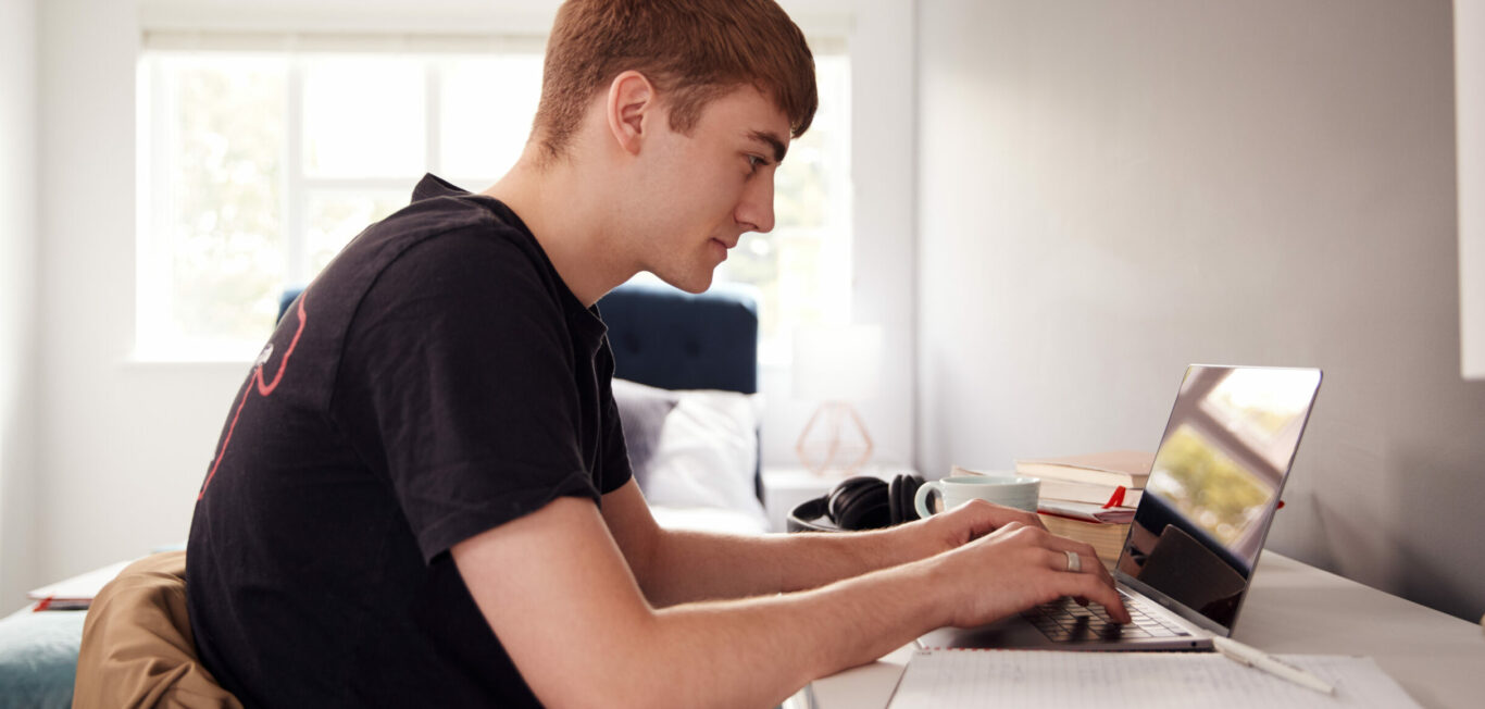 Male College Student In Shared House Bedroom Studying Sitting At Desk